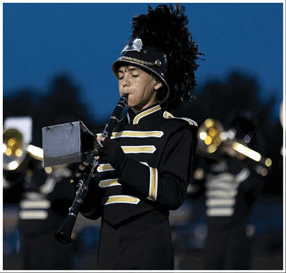 A person in a black and gold marching band uniform with a feathered hat is playing a clarinet outdoors during dusk. Description generated by AI