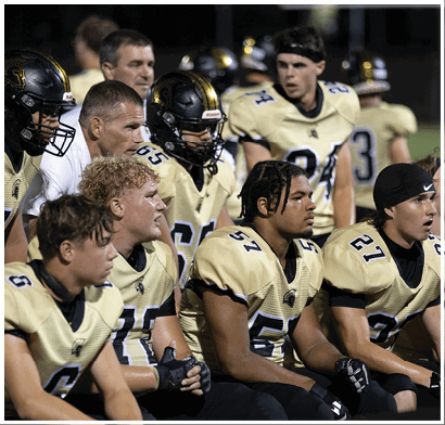 People wearing football helmets and uniforms are gathered closely together, likely during a game or practice. Description generated by AI