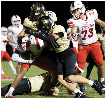 Two people wearing football uniforms and helmets are engaged in a physical tackle during a game. Description generated by AI