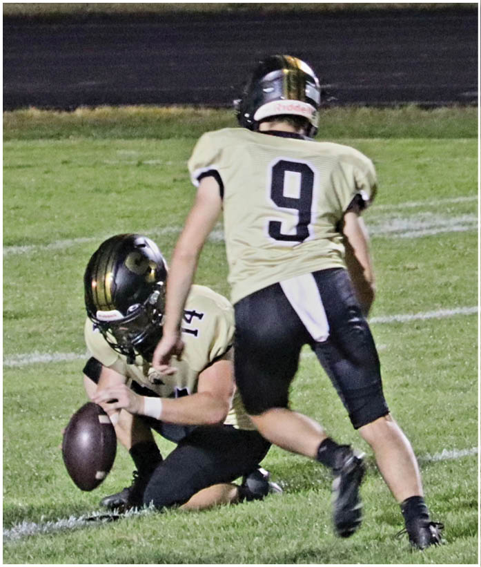 A person wearing a black and gold football helmet is crouched on a grassy field. Description generated by AI