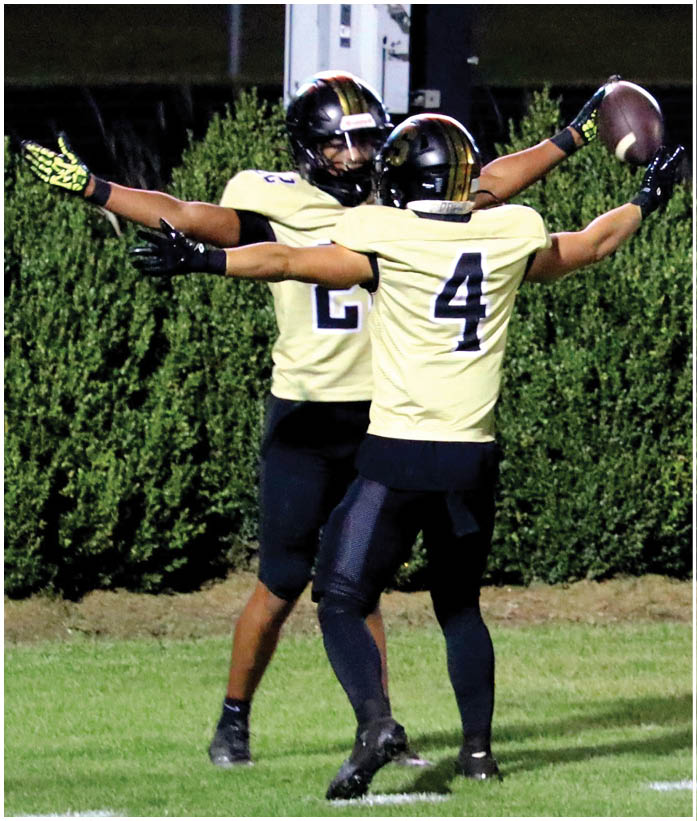 A person wearing a sports uniform with the number 2 is extending their arms forward against a background of dense green foliage. Description generated by AI