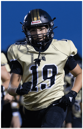 A person wearing a football uniform with the number 19 is running on a field with other players in similar uniforms visible in the background. Description generated by AI
