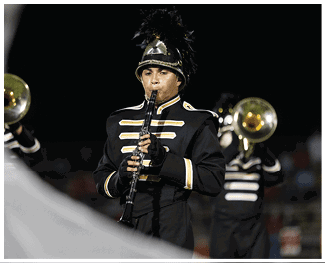A person wearing a black and gold marching band uniform is playing a clarinet during a nighttime performance. Description generated by AI