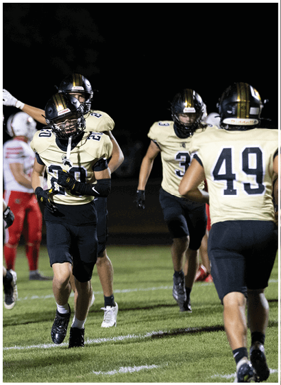 People wearing football uniforms are on a field at night with some players in black and gold and others in red and white. Description generated by AI