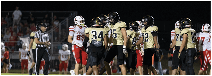 People wearing football uniforms and a referee are standing on a field during a game. Description generated by AI