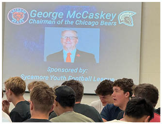 A presentation slide displays the name George McCaskey as Chairman of the Chicago Bears with logos of the Chicago Bears and another sports team, along with a photo of a senior person wearing glasses, a suit, and an orange tie. Description generated by AI