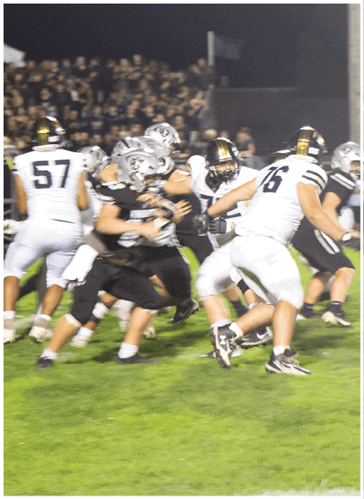 People wearing football uniforms are engaged in a nighttime game on a grass field with a crowd visible in the background. Description generated by AI