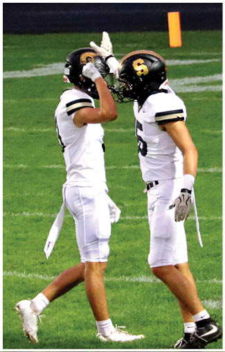 Two people wearing white football uniforms are standing on a grass field. Description generated by AI