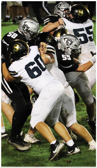 Several people wearing football uniforms are engaged in a close physical struggle on a grassy field during a game. Description generated by AI
