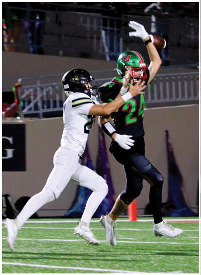 Two people in football uniforms are actively competing on a field, with one person in black and green holding a football and the other in white attempting to block or tackle. Description generated by AI
