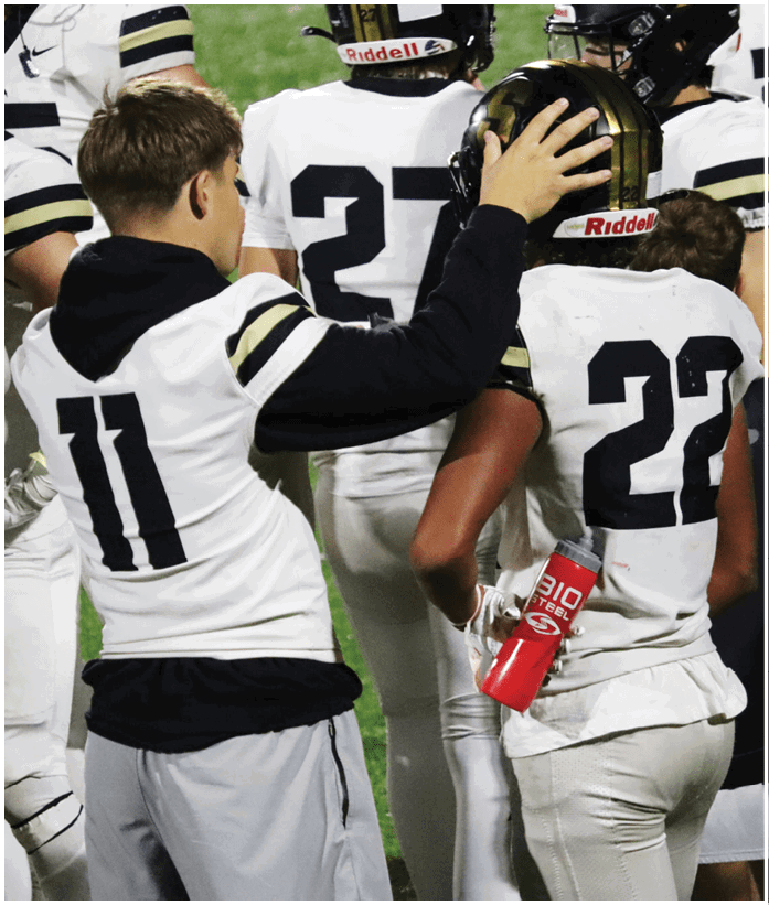 A person wearing a white sports jersey with the number 11 is standing among other people in white sports uniforms, one holding a red water bottle. Description generated by AI