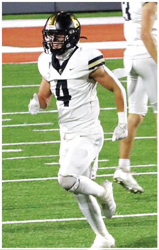 Two people wearing white football uniforms and helmets are on a football field with green turf and orange and white markings. Description generated by AI