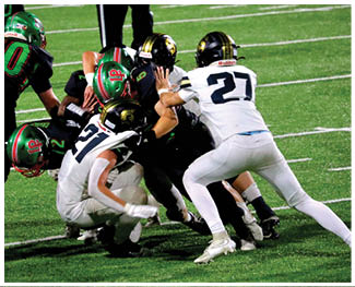 Several people in football uniforms are engaged in a close tackle on a green field during a game. Description generated by AI