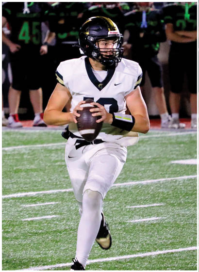 A person in a white sports uniform and helmet is in the foreground while several people in black and green football uniforms stand with arms crossed in the background on a sports field. Description generated by AI