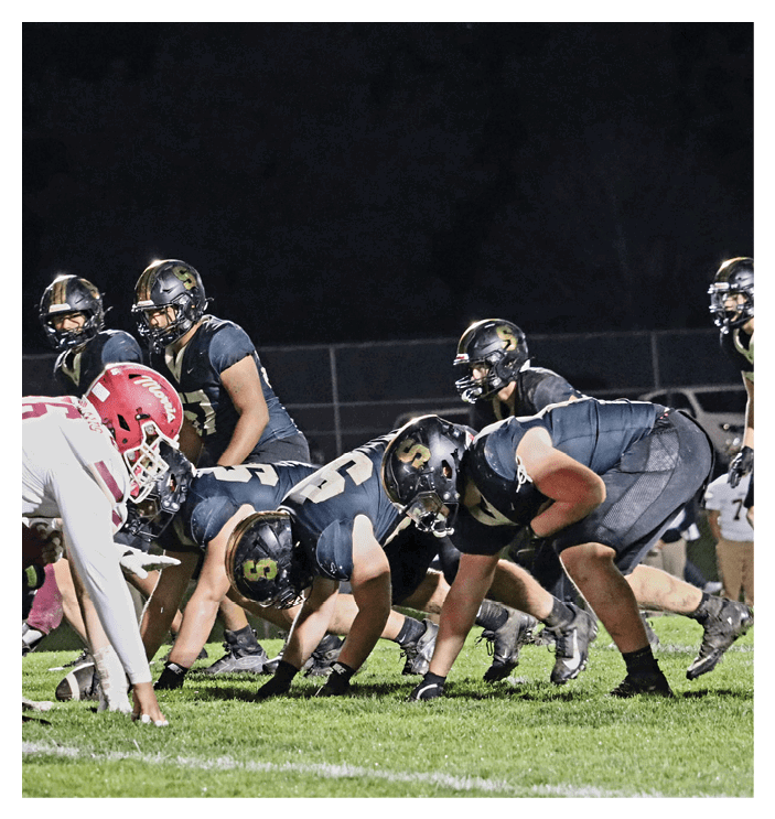 A football game is in progress with players on the field. One player is throwing a football while another player is trying to catch it. The players are wearing uniforms and are actively engaged in the game. AI generated content