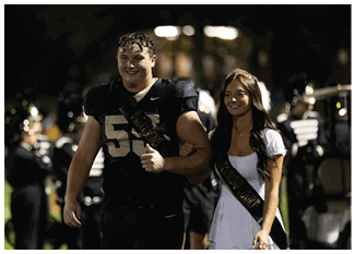 A person wearing a football uniform with the number 55 and a sash that reads “HOMECOMING COURT" is smiling and giving a thumbs up. Description generated by AI