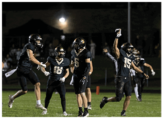 A group of people wearing black football uniforms are celebrating on a well-lit field at night. Description generated by AI