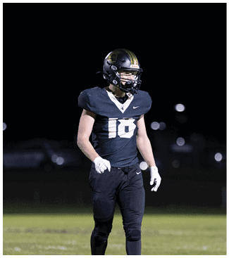 A person wearing a black football uniform with the number 16 and a helmet is standing on a field at night. Description generated by AI
