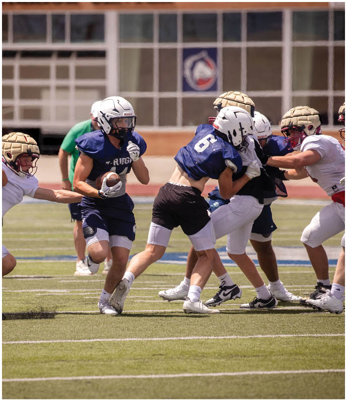 Three football players in blue and white uniforms running on a field. Description generated by AI