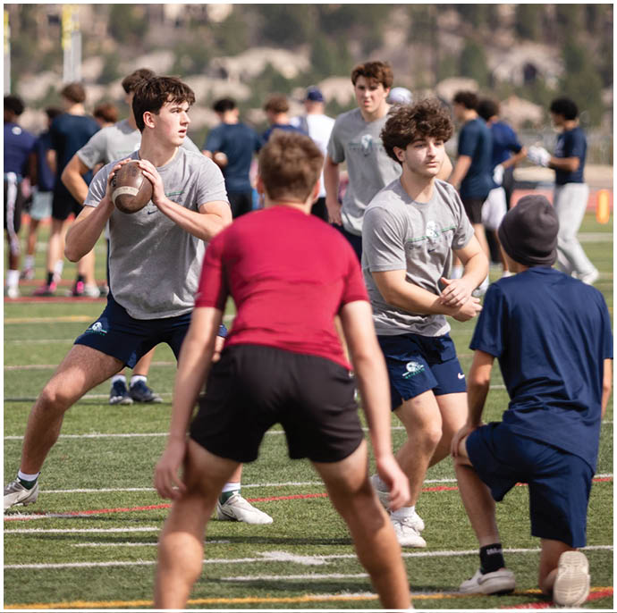 Three football players in blue and white uniforms running on a field. Description generated by AI