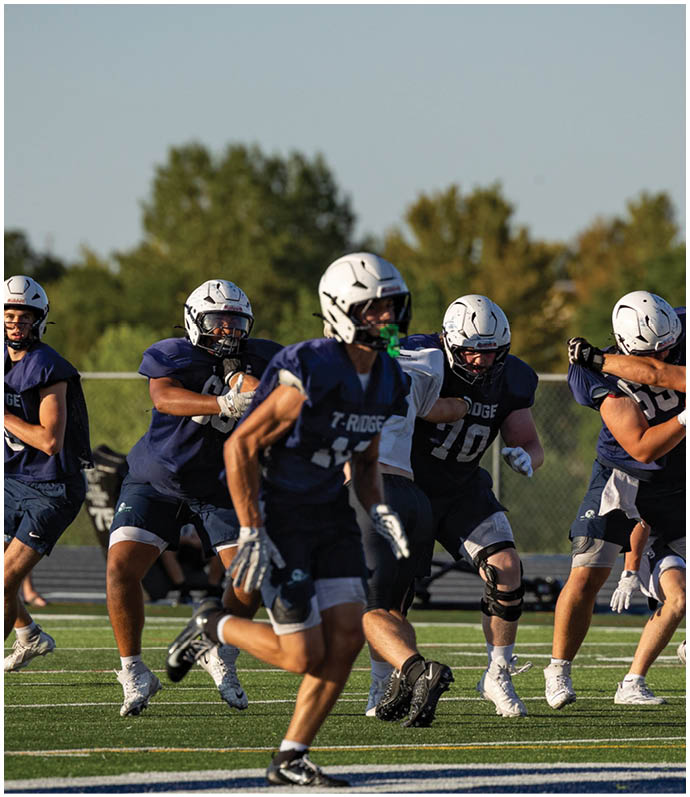 Three football players in blue and white uniforms running on a field. Description generated by AI