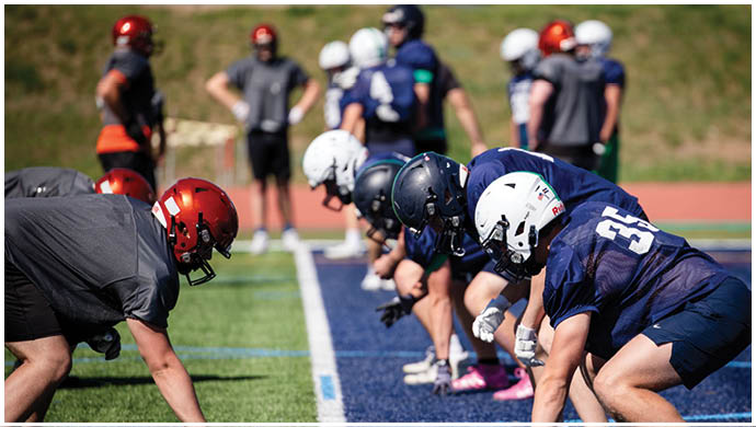 Three football players in blue and white uniforms running on a field. Description generated by AI