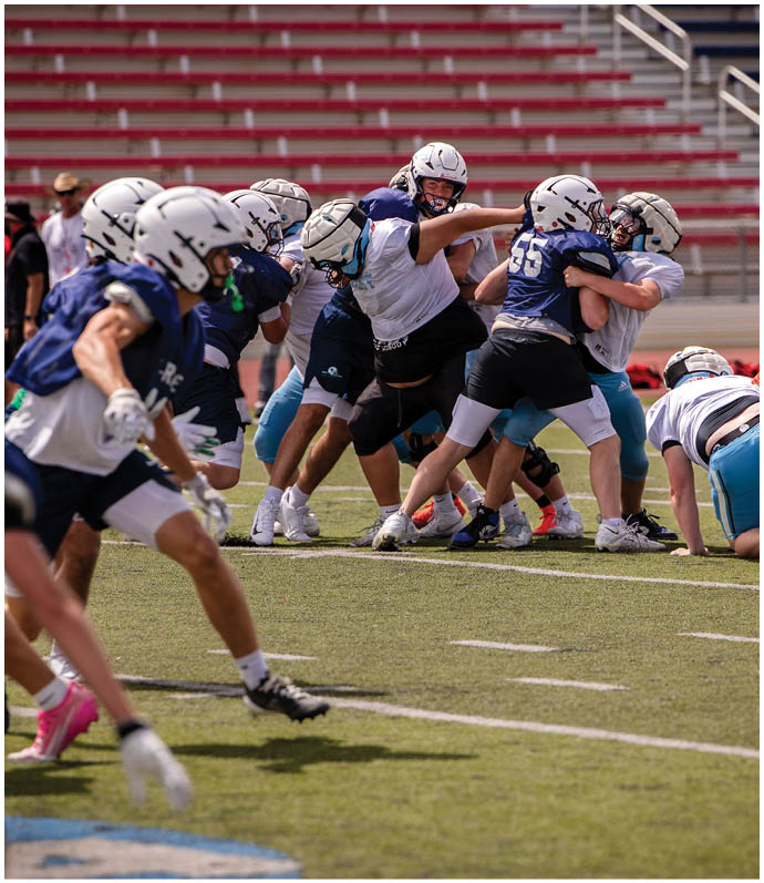 Three football players in blue and white uniforms running on a field. Description generated by AI