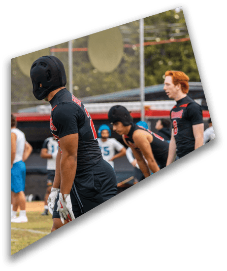 A group of people wearing black football uniforms with helmets are gathered on a field at night, with some of them interacting closely. Description generated by AI