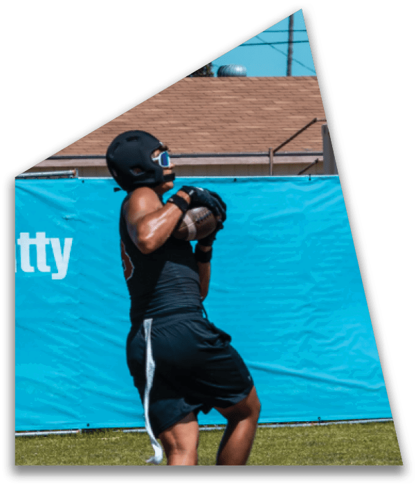 A person wearing a black football uniform and helmet is holding a football and appears to be preparing to run on a brightly lit field with blurred players in the background. Description generated by AI