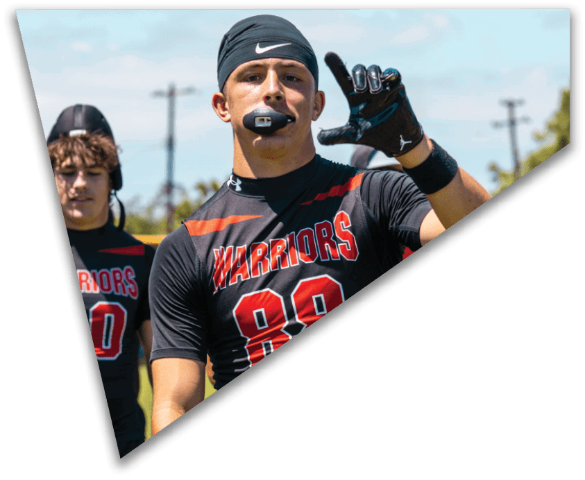 A group of football players in black uniforms are lined up on the field preparing for a play while players in white uniforms stand in the background. Description generated by AI