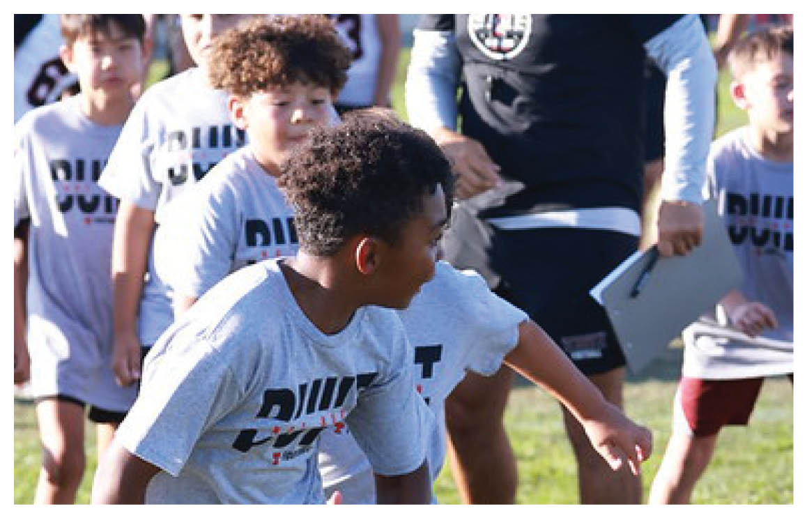 A football game is in progress with players on the field. One player is throwing a football while another player is trying to catch it. The players are wearing uniforms and are actively engaged in the game. AI generated content