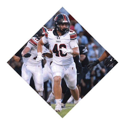 A football player wearing a black jersey with the number 10 sits on the ground with a football helmet on the ground next to him. AI generated content