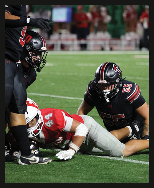 A person with curly hair wearing a black football uniform with “VISTA" on the jersey is sitting on a grassy field with one leg bent and the other extended. Description generated by AI