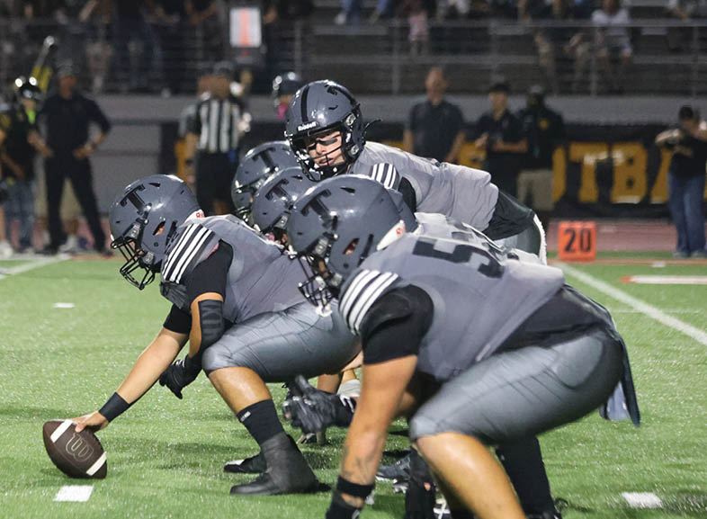 Four people wearing black football uniforms with “VISTA" on the front are standing together in a stadium with a crowd in the background, two of them holding helmets raised above their heads. Description generated by AI