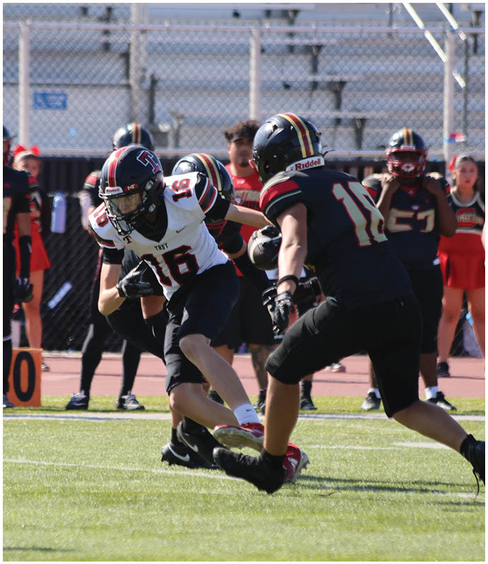 Three football players in blue and white uniforms running on a field. Description generated by AI