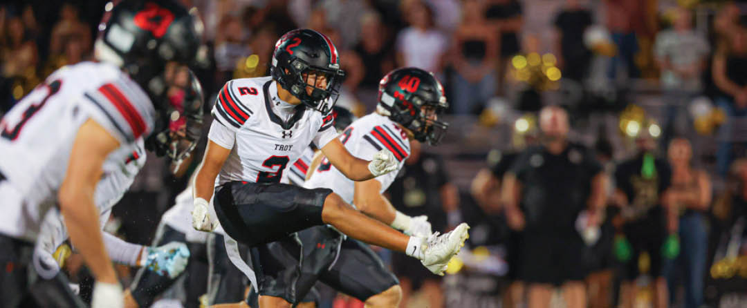 Four people wearing black sports jerseys with “VISTA" on them stand closely together in front of a large crowd, with one person raising an arm in celebration. Description generated by AI