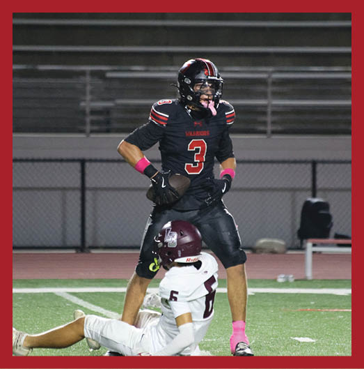A person wearing a black football uniform with “VISTA" on the jersey is sitting on a grassy field with one leg bent and the other extended, next to a black football helmet. Description generated by AI