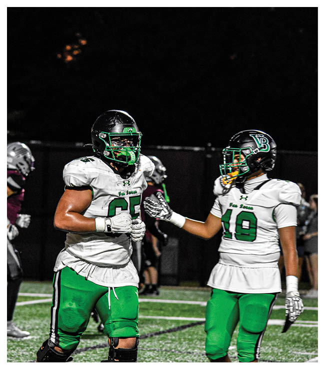 A football game is in progress with players on the field. One player is throwing a football while another player is trying to catch it. The players are wearing uniforms and are actively engaged in the game. AI generated content