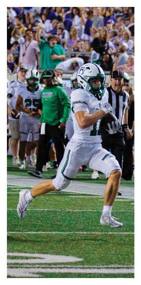 A football player is kneeling on the field, wearing a green jersey and a helmet. AI generated content