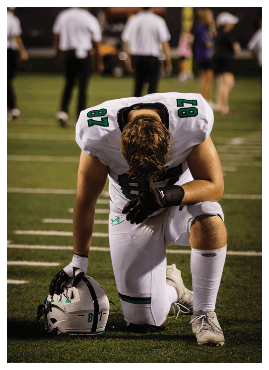 A football player wearing a helmet and white uniform is holding his helmet above his head. AI generated content