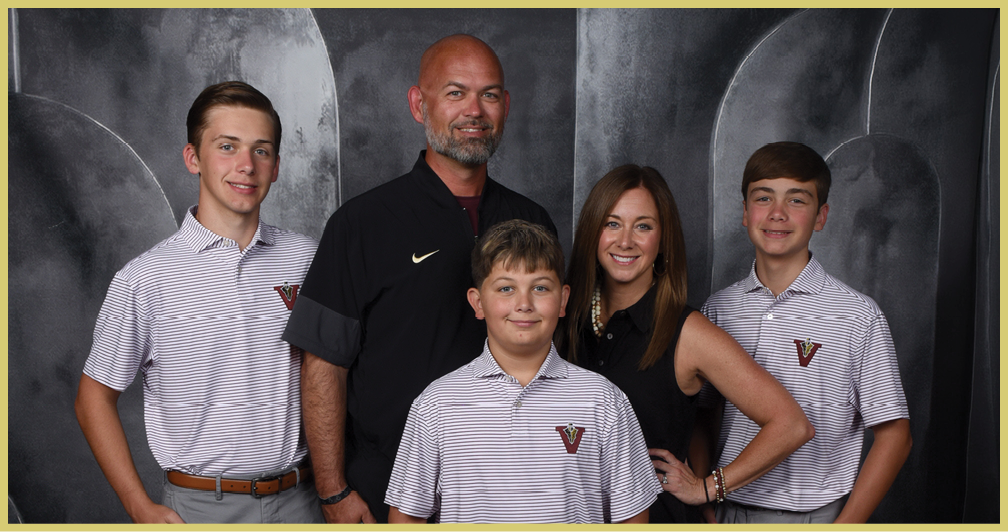 Five people wearing matching striped polo shirts and one person in a black shirt pose together against a dark, textured backdrop. Description generated by AI