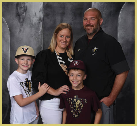 A group of four smiling people, two adults and two children, wearing matching sports-themed clothing with a “V" logo, posing together against a dark backdrop. Description generated by AI
