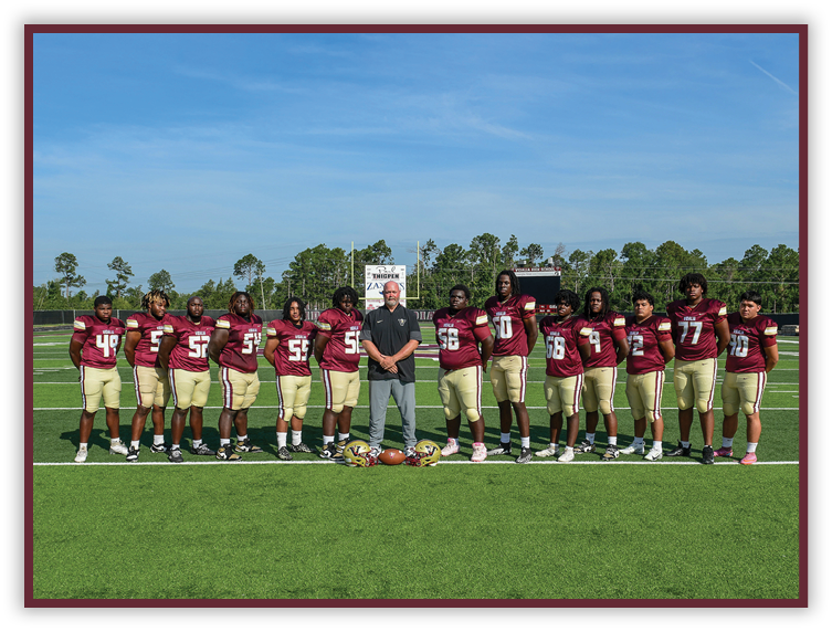 A group of people wearing maroon and gold football uniforms stand in a line on a football field with a coach in casual clothing standing in the center. Description generated by AI