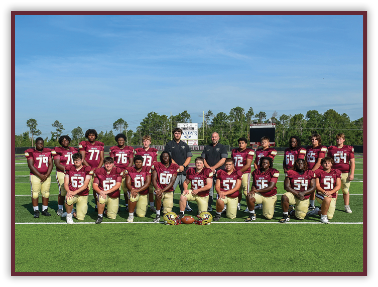 A group of people wearing maroon and gold football uniforms pose together on a green field with a clear blue sky in the background. Description generated by AI