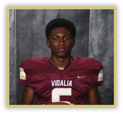 A person wearing a maroon football jersey with the word Vidalia and the number 5 stands against a gray textured backdrop. Description generated by AI