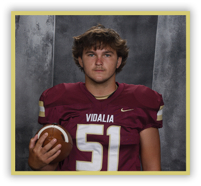 A person with long dreadlocks wearing a maroon football jersey with the number five and the word Vidalia is holding a football against a gray textured background. Description generated by AI
