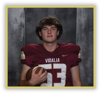 A person with medium-length hair wearing a maroon football jersey with the number 53 and the word Vidalia is holding a football against a dark textured background. Description generated by AI