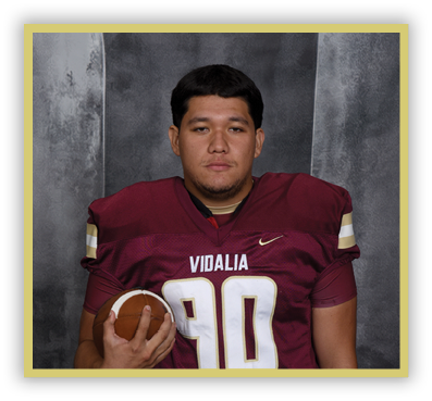 A person wearing a maroon football jersey with the number 90 and the word Vidalia is holding a football against a gray backdrop. Description generated by AI