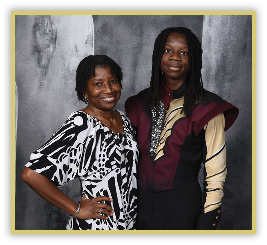 Two people stand closely together smiling, one wearing a black and white patterned dress and the other wearing a maroon and beige costume with decorative details. Description generated by AI