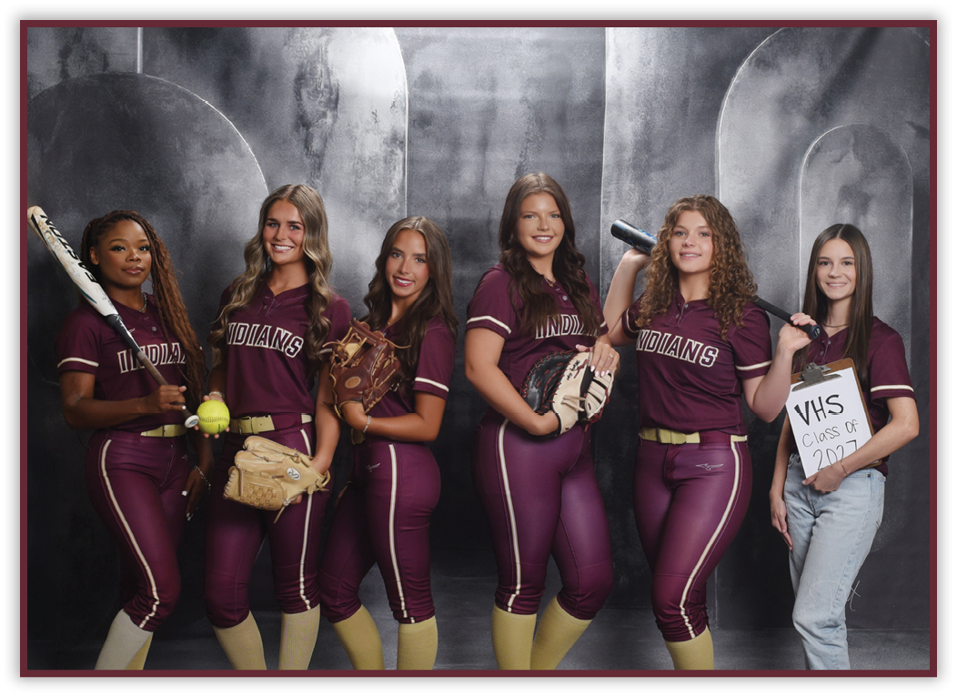 Six people wearing matching maroon softball uniforms and holding softball equipment pose together in front of a gray backdrop, with one person holding a sign that reads “VHS Class of 2024." Description generated by AI